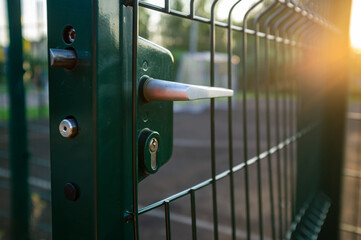 Handle with a lock on the open gate of a sports ground fenced with a welded mesh fence, outdoors,...