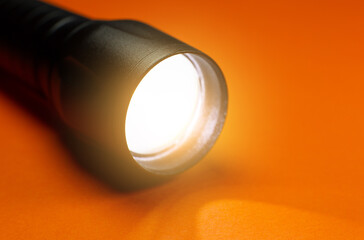 Black Flashlight and a ray of light on the orange background. Close up photo.
