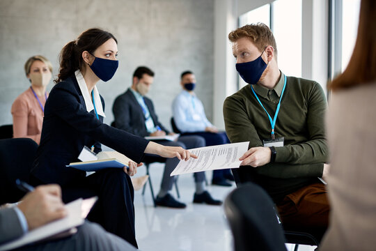 Business colleagues wearing face masks while talking about seminar schedule at conference hall.