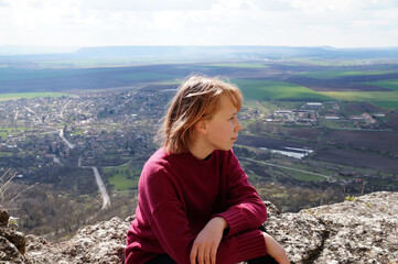 teenage girl sitting on top of a mountain and looking thoughtfully into the distance