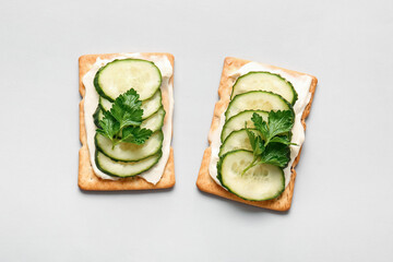 Tasty crackers with cheese and cucumber on grey background