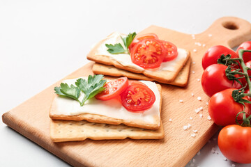 Board with tasty crackers and tomatoes on grey background, closeup