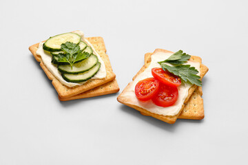 Tasty crackers with cheese, tomatoes and cucumber on grey background