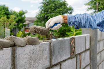 Masonry worker make concrete wall by cement block and plaster at construction site.
