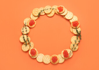 Frame made of tasty crackers with red caviar and thyme on color background