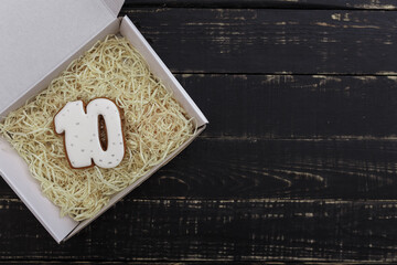 Number 10 shape gingerbread cookie on present box on black wooden table background. Number ten concept. Place for text.