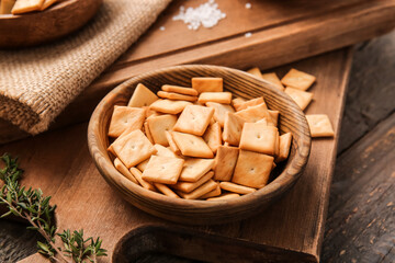Bowl with tasty crackers on wooden background, closeup