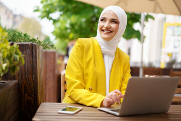 Beautiful smiling muslim woman with laptop at cafe