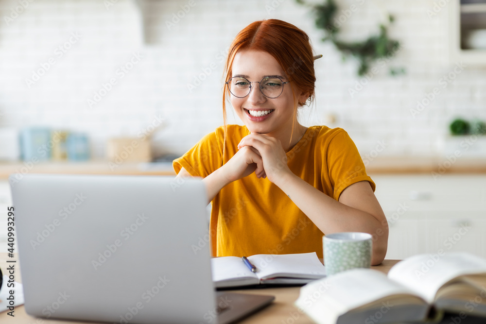 Wall mural Online learning, portrait of red-haired happy caucasian female freelancer or smiling woman student using a laptop for a video call with a teacher, distance education concept