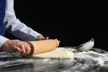 Woman rolling out dough on dark background