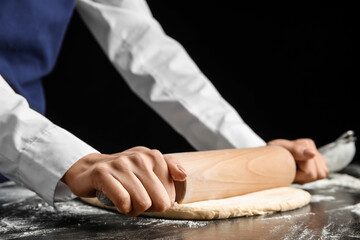 Obraz na płótnie Canvas Woman rolling out dough on dark background