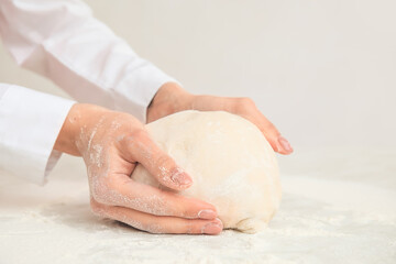 Woman kneading dough on light background