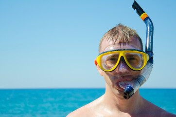 Caucasian man in mask with snorkel against background of blue sky and turquoise sea is ready to dive. Aquatic recreation concept. Adult male is resting on seashore on summer vacations with copy space.