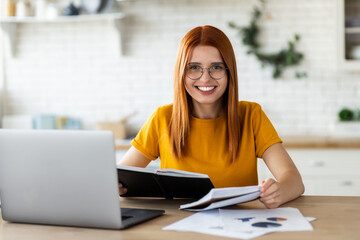 Online learning, portrait of beautiful red-haired young female student with laptop and notepad,...
