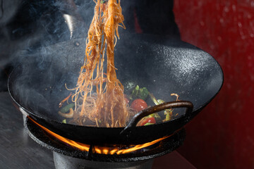 Funchoza flambe rice noodles with vegetables cooking on fire in wok pan. Street food.