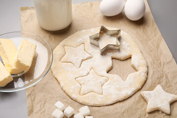 Parchment with uncooked cookies and ingredients on grey background