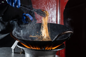 Funchoza rice noodles with vegetables cooking on fire in wok pan. Street flambe food