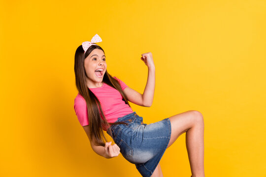 Photo of charming funny school girl wear pink t-shirt rising fists looking empty space smiling isolated yellow color background