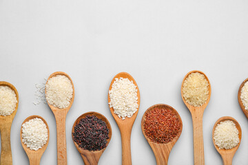 Spoons with different types of raw rice on light background
