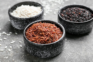 Bowls with different types of raw rice on grunge background