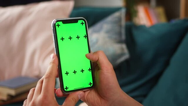 Close-up of smartphone with green screen, young man hands holding mobile phone, zoom in, isolate display, touch screen, chroma key phone concept, surfing the internet with gadgets. 