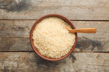Bowl with raw rice on wooden background