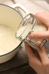 Female hands and jar with raw rice on wooden background, closeup