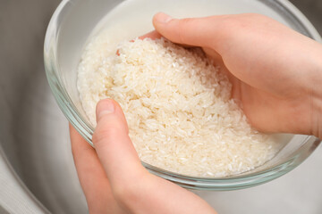 Woman rinsing rice in glass bowl under running water, closeup