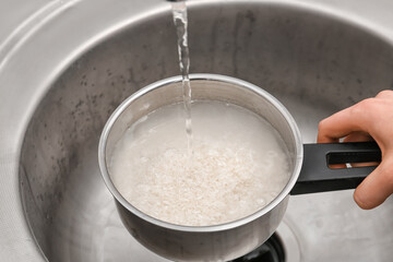 Woman rinsing rice in saucepan under running water