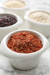 Bowls with different types of raw rice on light background, closeup