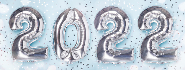 Silver balloons in the form of numbers 2022 and confetti stars on blue background. Happy New Year concepts