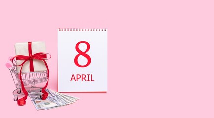 A gift box in a shopping trolley, dollars and a calendar with the date of 8 april on a pink background.