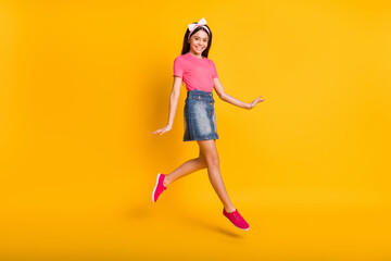Fototapeta na wymiar Photo of adorable cute small schoolgirl dressed pink t-shirt jumping high walking smiling isolated yellow color background