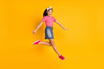 Photo of impressed shiny school girl wear pink t-shirt smiling jumping high isolated yellow color background