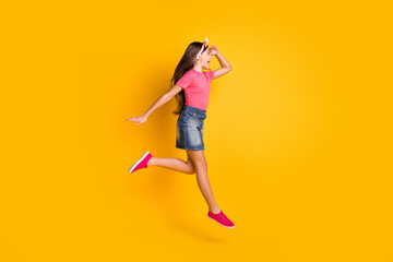 Fototapeta na wymiar Photo of cute funky schoolgirl dressed pink t-shirt jumping high smiling arm forehead looking empty space isolated yellow color background