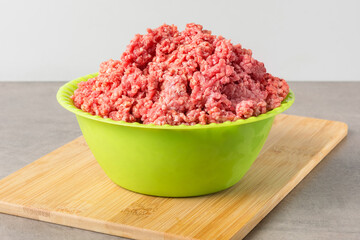 Chopped minced meat in a green plastic plate on a cutting wooden board