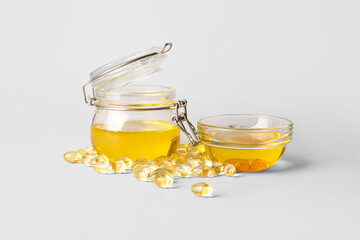 Jar and bowl with fish oil and capsules on light background
