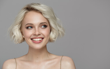 Portrait of a beautiful smiling blonde girl with a short haircut. Gray background. - 440998877