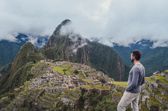 Young man standing, contemplating Machu Picchu lost city with Huayna Picchu mountain. Ruins of ancient inca civilization in the sacred valley of Cusco Province. Peru, South America