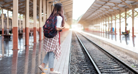 Young asian woman traveler with backpack in the railway, Backpack and hat at the train station with a traveler, Travel concept. Woman traveler tourist walking at train station