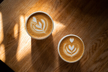Two cups of fresh coffee with latte art on wooden table in sunlight. Morning cappuccino with hearts...