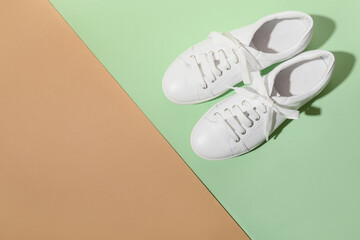 White female gumshoes for sport outfit on beige and green color background with copy space. View from above.