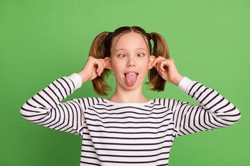 Photo of cute childish small schoolgirl dressed striped sweater showing tongue big ears looking nose isolated green color background