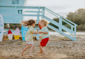 Boy and girl playing at the sand beach against lifeguard tower with surfboards.