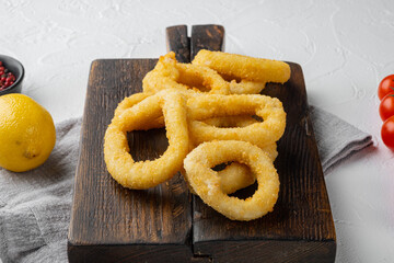 Crunchy deep fried squid or onion rings in batter, on serving board, on white stone table background