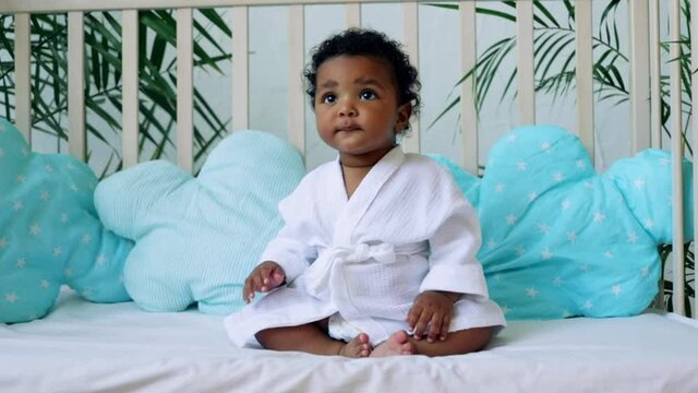 cheerful smiling baby boy American-African plays on the bed in a white robe after bathing, hygiene and child care concept