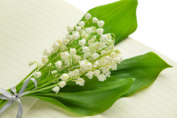 Obraz premium Beautiful lily-of-the-valley flowers and notebook on white background, closeup