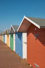 Fototapeta na wymiar Brightly coloured beach huts with diminishing perspective against a clear blue sky.