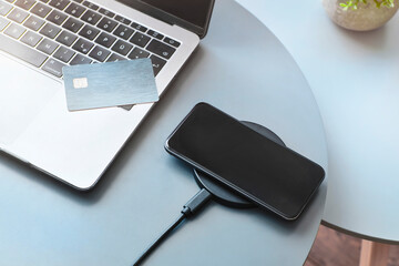 Using wireless charger to recharge smartphone battery next to laptop. Electronic chip access card. - obrazy, fototapety, plakaty