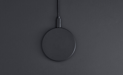 High angle view of black plastic circular wireless charger laying on dark grey desk.